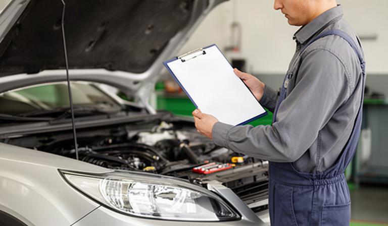 Mechanic reviewing a used car inspection checklist beside a vehicle