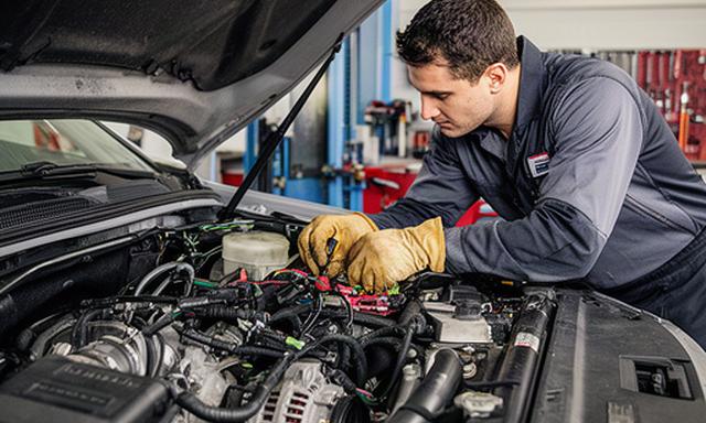 Mechanic inspecting alternator and starter connections in a vehicle engine bay